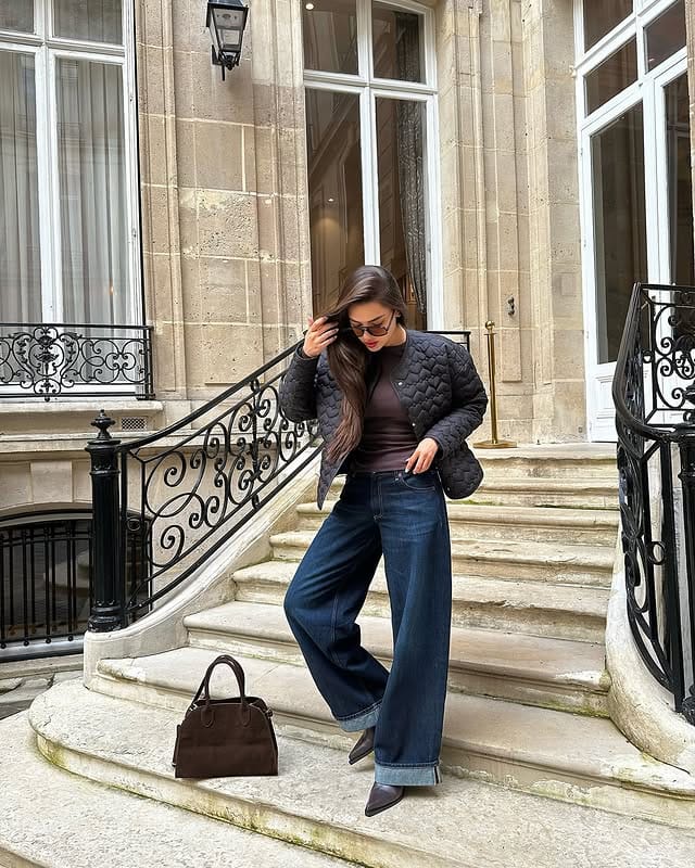 Woman wearing a leather jacket, sunglasses and wide-leg pants, posing on the steps of a classic building in São Paulo, sophisticated casual fashion.