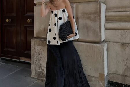 Stylish woman wearing sunglasses, a cute polka dot dress, and wide leg pants posing on the street in front of a building with a fast track assessment sign.